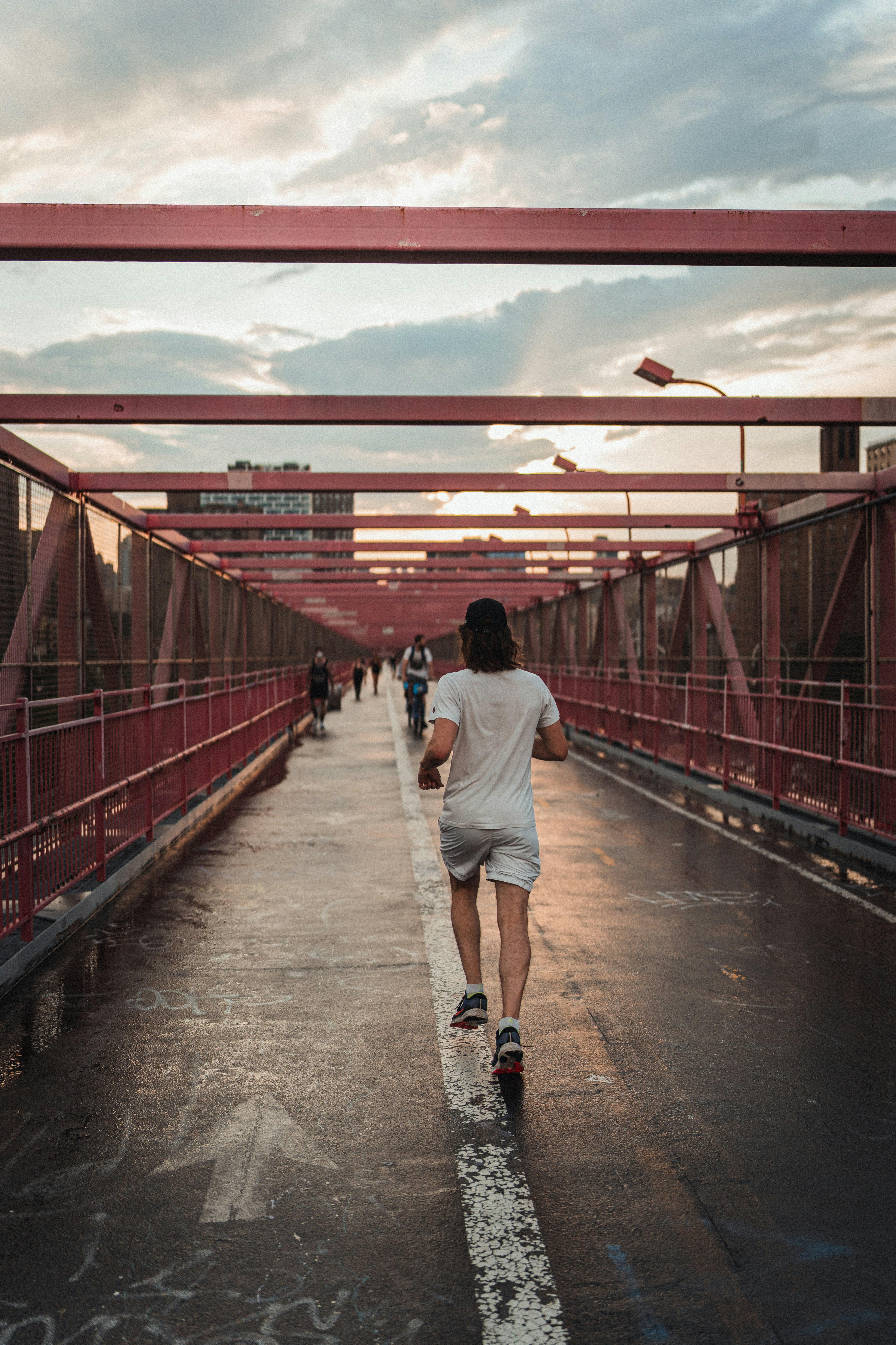 man in white t-shirt and brown pants walking on red bridge during daytime